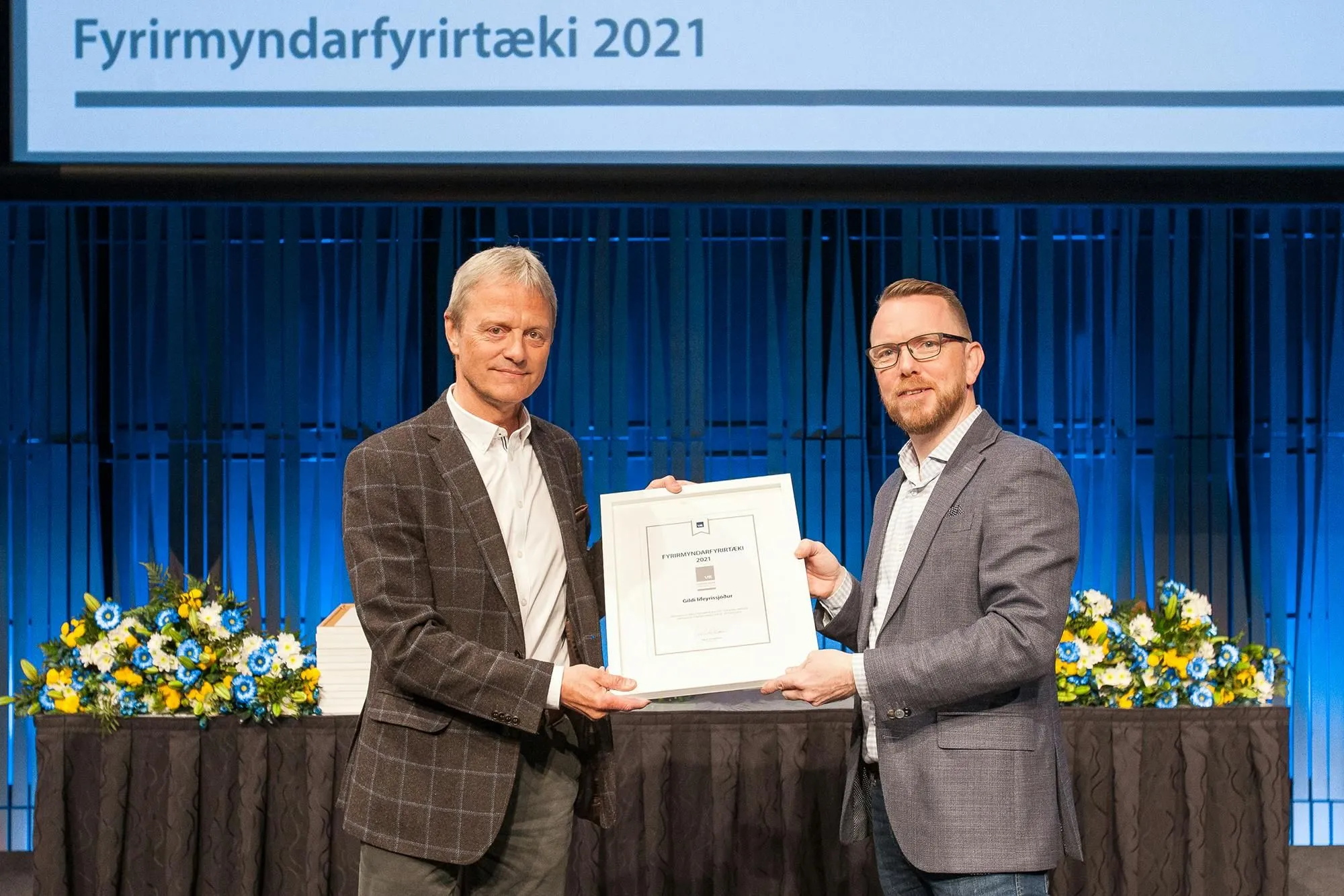 Viðurkenning afhent á sviði undir skjá sem á stendur Fyrirmyndarfyrirtæki 2021